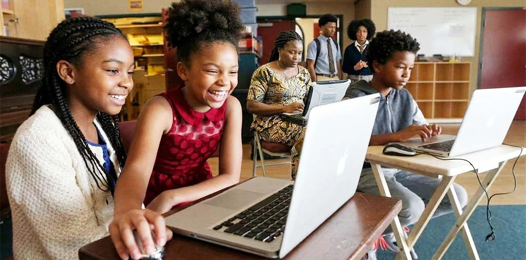 Des élèves rient devant un ordinateur portable en classe