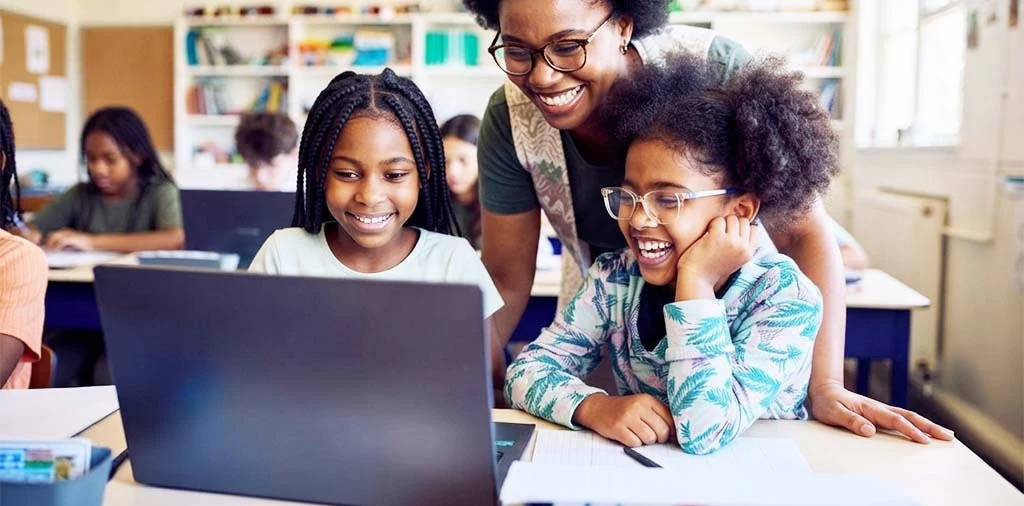 Une enseignante accompagne deux élèves sur ordinateur